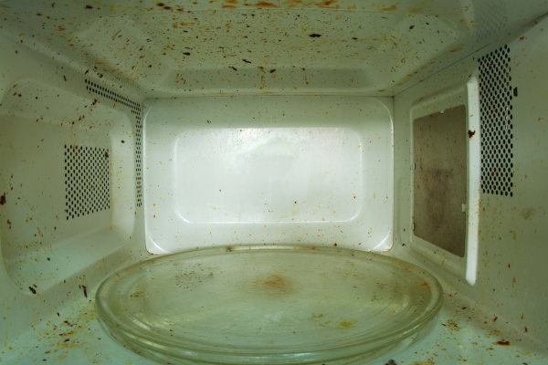 The interior of a microwave oven is heavily soiled with food splatters and residue, particularly on the walls and glass turntable. This image illustrates a common cause of unpleasant odours in microwaves, which Quality Appliance Repairs (QAR) addresses in their maintenance and cleaning tips for keeping appliances fresh and functional.