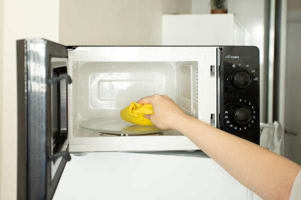A person uses a yellow cloth to wipe down the interior of a clean microwave oven. This step is part of a regular maintenance routine often recommended by Quality Appliance Repairs (QAR) to keep microwaves in optimal condition and free from odours or residue build-up.
